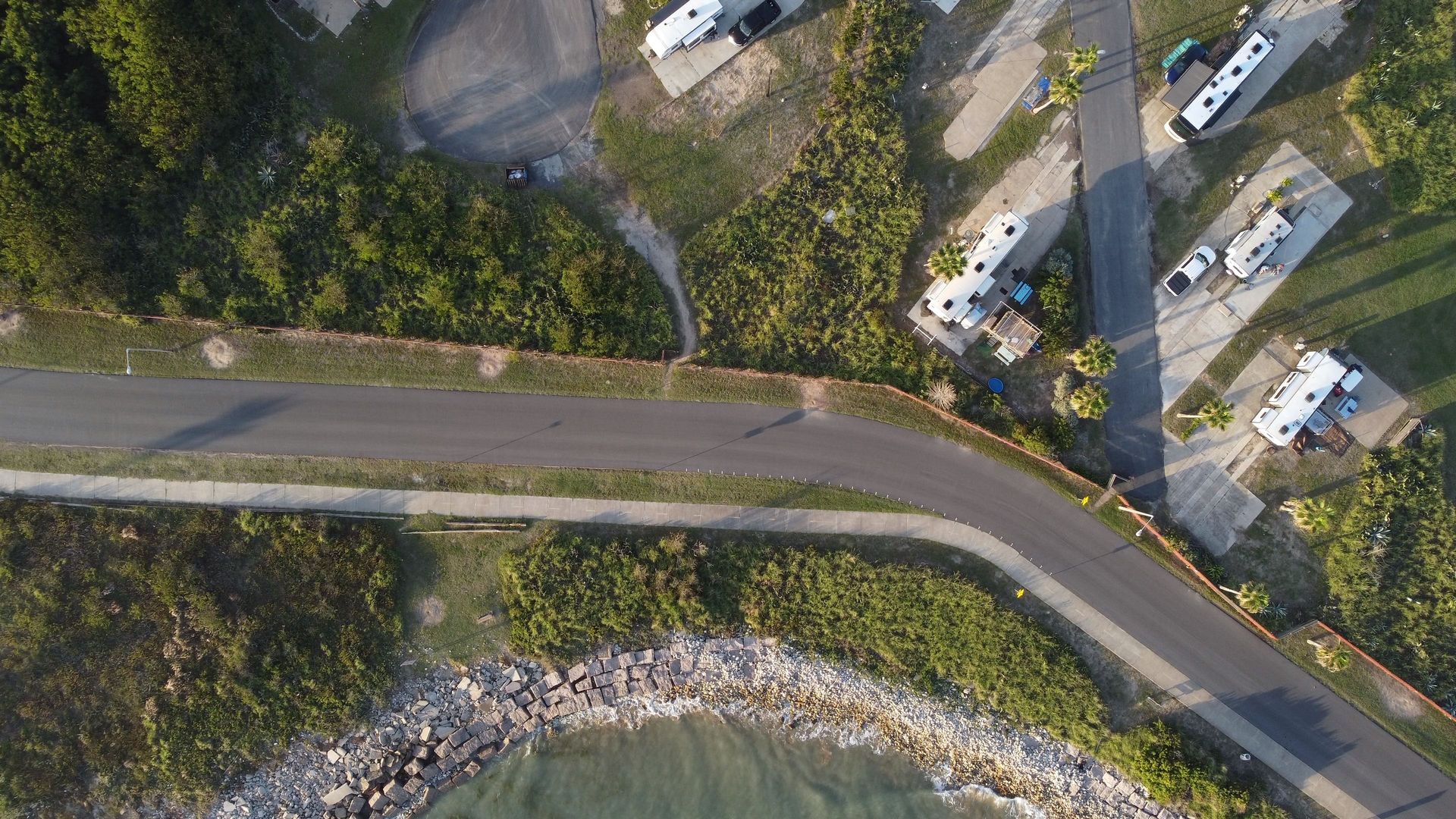 Drone shot of a coastal campground and road beside the shoreline and trees.