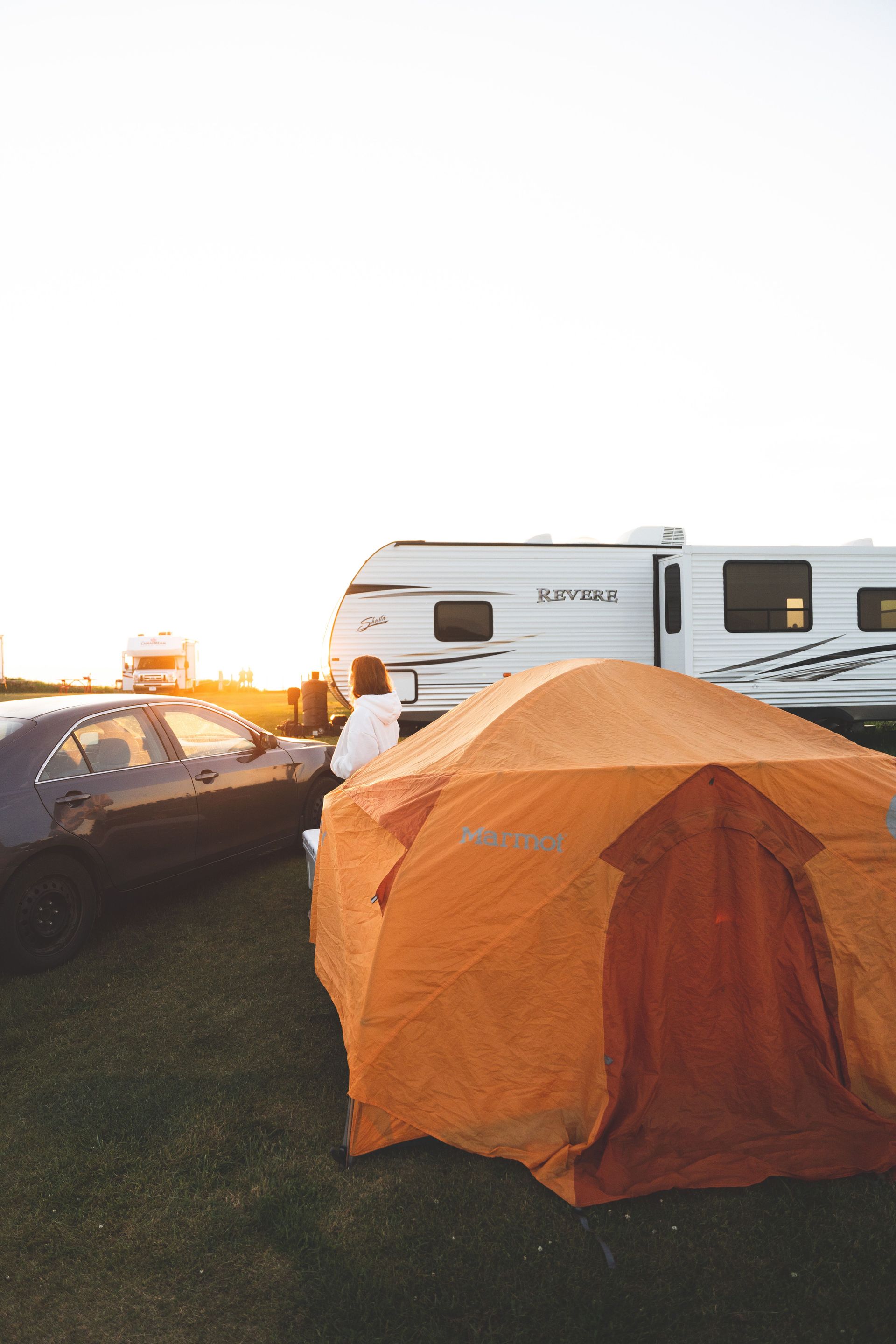 A serene camping scene with an orange tent and RV at sunset, ideal for adventure seekers.